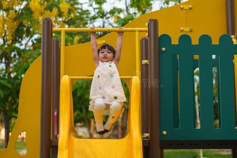 Glückliches Kleinkind, das die gelbe Bar an der Hand am Spielplatz im Park im Freien hängt stockfotografie
