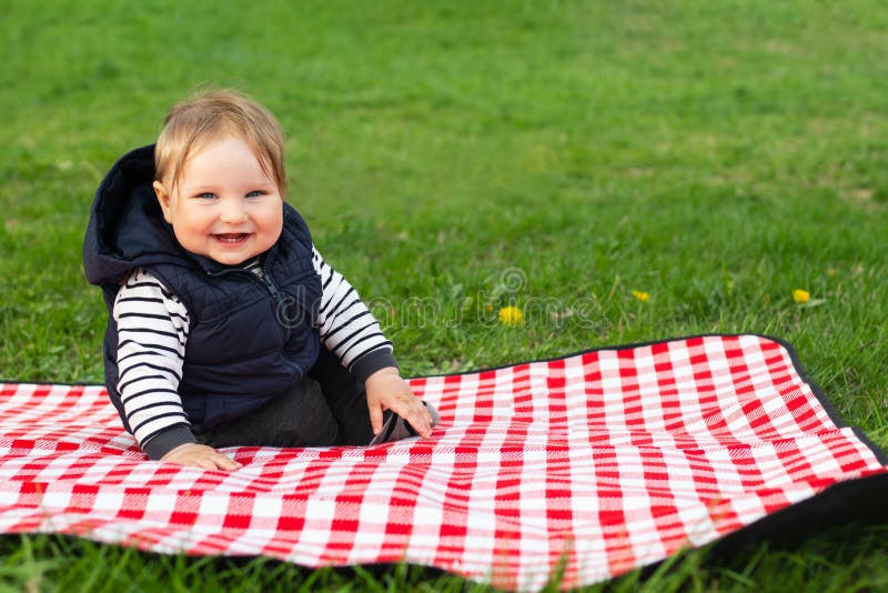 Glückliches lachendes Kind auf Decke draußen sitzen. Frühjahr. Textzeichenplatz lizenzfreies stockfoto