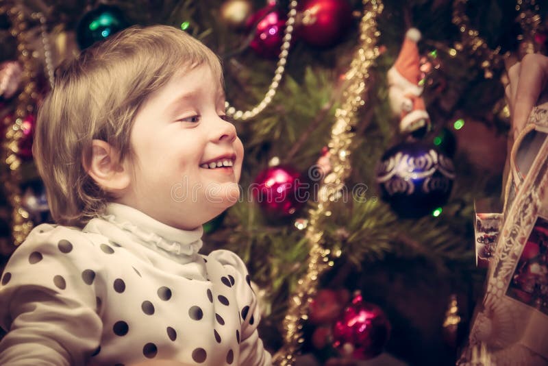 Glückliches lächelndes Kind, das Weihnachtsgeschenk mit Weihnachtsbaum auf Hintergrund im Retrostil erhält lizenzfreies stockbild Glückliches lächelndes Kind, das Weihnachtsgeschenk mit Weihnachtsbaum auf Hintergrund im Retrostil erhält lizenzfreies stockbild