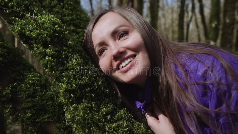 Glückliches Mädchen berührt das weiche starke grüne Moos auf dem Baum mit ihrem Gesicht