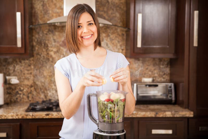 Beautiful young Hispanic woman using some fruits and vegetables to make a healthy juice and smiling. Beautiful young Hispanic woman using some fruits and vegetables to make a healthy juice and smiling