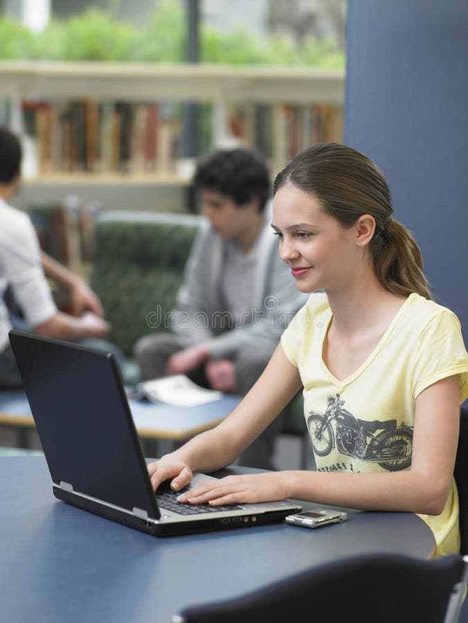 Glückliches Mädchen, das Laptop in der Bibliothek verwendet stockfotos Glückliches Mädchen, das Laptop in der Bibliothek verwendet stockfotos