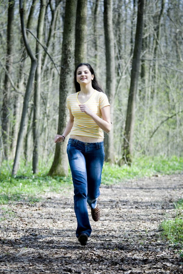 Happy young woman with long, dark hair, running down a forest path, toward the camera. Wearing a short-sleeved yellow shirt and blue jeans. Happy young woman with long, dark hair, running down a forest path, toward the camera. Wearing a short-sleeved yellow shirt and blue jeans.