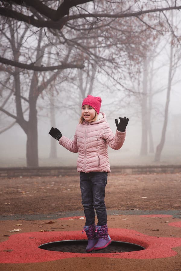 Glückliches Mädchen in einer rosa Jacke, die draußen auf die Trampoline in Park springt Herbst, nebelhafter Wald lizenzfreie stockbilder Glückliches Mädchen in einer rosa Jacke, die draußen auf die Trampoline in Park springt Herbst, nebelhafter Wald lizenzfreie stockbilder