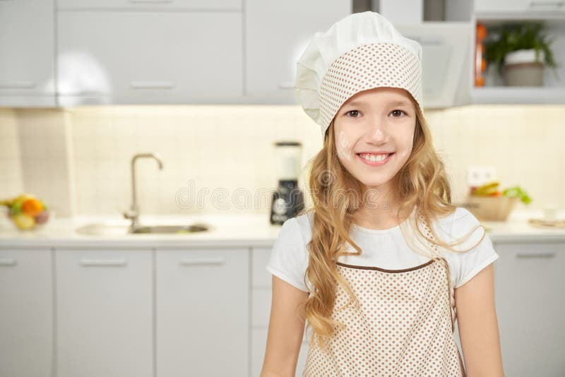 Glückliches Mädchen im Schutzblech- und Chefhut, der in der Küche aufwirft stockfotos Glückliches Mädchen im Schutzblech- und Chefhut, der in der Küche aufwirft stockfotos