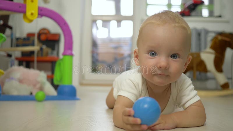 Glückliches nettes Kleinkind mit Spielzeug in den Händen betrachtet Kamera und kriecht Vorwärtsnahaufnahme zuhause