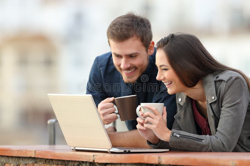 Glückliches Paar, das Laptopinhalt auf einem Balkon überprüft