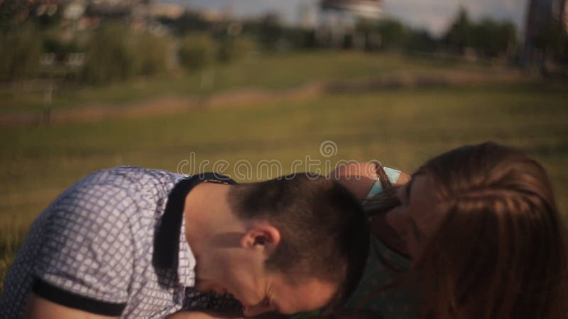 Glückliches Paar im Liebeslachen und haben Spaß auf einem Datum Kerl und Mädchen auf grünem Gras auf Stadthintergrund stock footage
