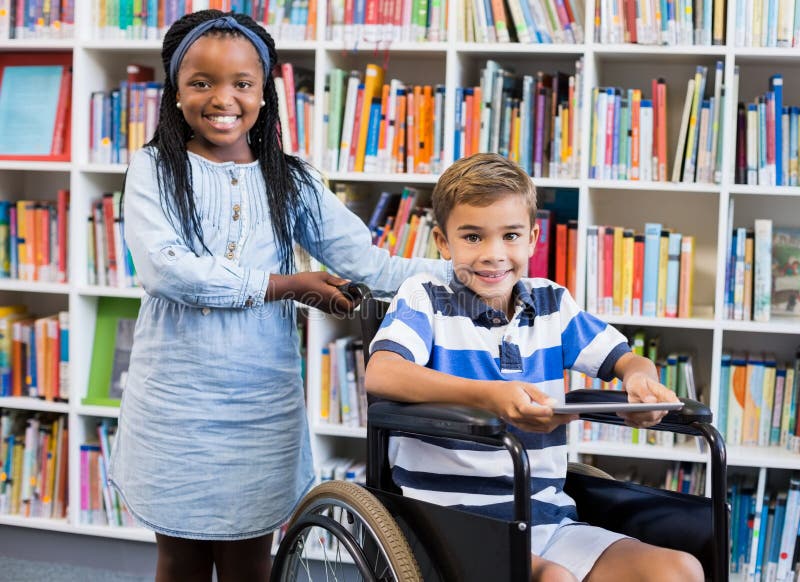 Glückliches Schulmädchen, das mit Schüler auf Rollstuhl steht