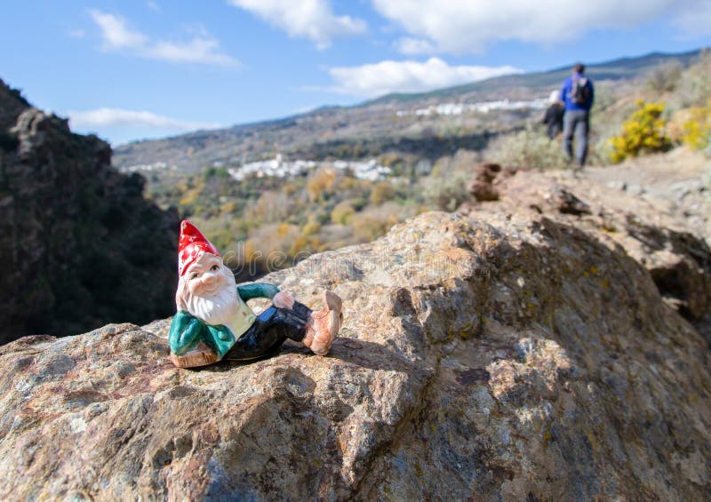 Gnome lying on a rock and in the background hikers and villages of La Taha in the Alpujarra of Granada