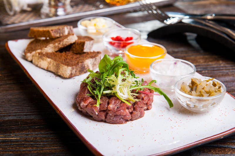 Gnälla tartare med arugulasallad, knapriga brödchiper, såser och mellanmål på den vita plattan på den tjänade som restaurangtabel arkivbilder Gnälla tartare med arugulasallad, knapriga brödchiper, såser och mellanmål på den vita plattan på den tjänade som restaurangtabel arkivbilder