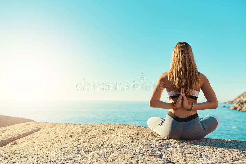 Go and find yourself. Rearview shot of a young woman practicing yoga on the beach. royalty free stock photography