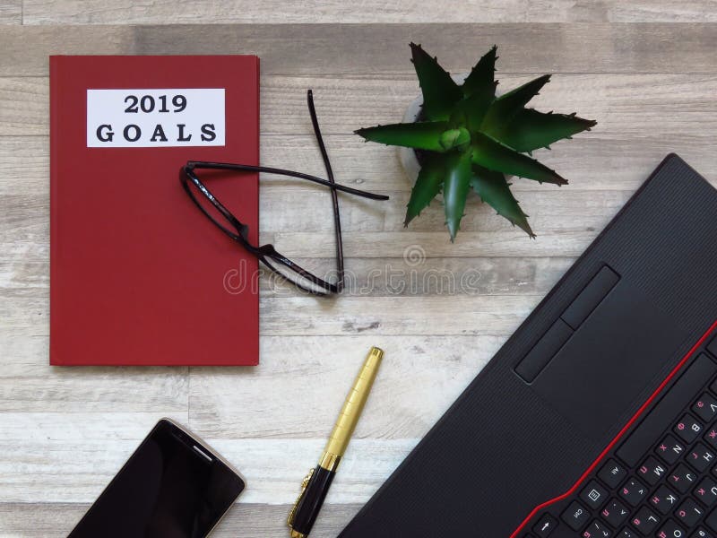 Goals for 2019. Office desk with 2019 goals note. Black laptop, golden colour mobile phone, golden luxurious pen, black frame spectacles, red notebook and flowers. Worktable. Top view. Future plans and goals. Business plans. Space for text. Goals for 2019. Office desk with 2019 goals note. Black laptop, golden colour mobile phone, golden luxurious pen, black frame spectacles, red notebook and flowers. Worktable. Top view. Future plans and goals. Business plans. Space for text.