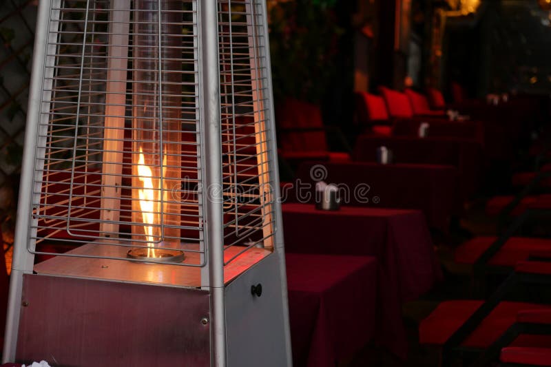 Godere di una piacevole esperienza di pranzo all'aperto con un riscaldatore a patio e un ambiente caldo. Un riscaldatore a patio brilla calorosamente in tavoli vuoti, invitando a un senso di comodità e di calore.