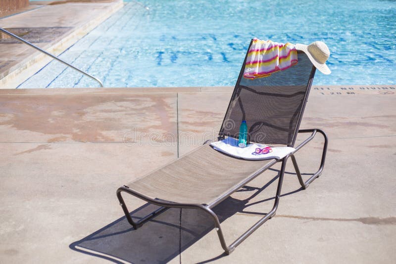 Lounge chair by a swimming pool with sunscreen and a towel