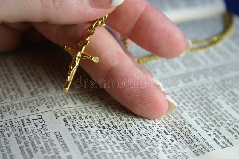 Hand holding gold crucifix on open bible pages