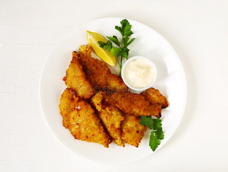 Golden batter deep fried fish fillets, served on white plate with sauce and lemon