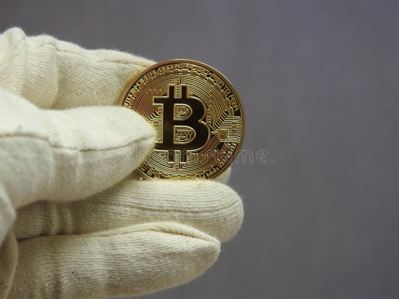Golden Bitcoin handled with gloves. stock images