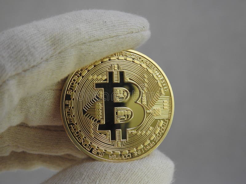 Golden Bitcoin handled with gloves. stock photo