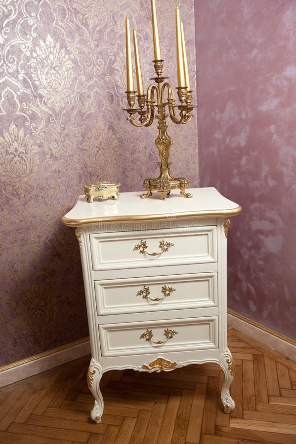 Golden candlestick with five candles on white wooden furniture in front of luxurious textured wall