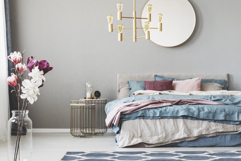 Golden chandelier above king size bed with blue, beige and pastel pink sheets