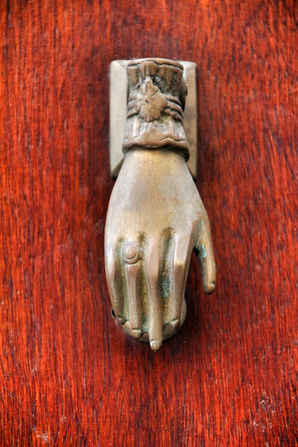 Golden doorknocker with hand shape on old wooden door