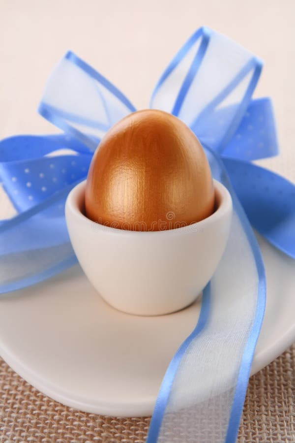 Golden easter egg in beige cup with blue bow