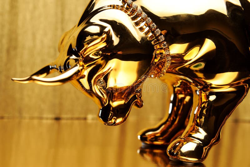 Golden figurine of a bull bowing its head on a gold background close-up.