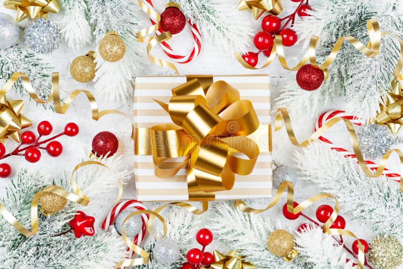 Golden gift or present box, snowy fir tree and christmas decorations on white wooden table top view. Flat lay.