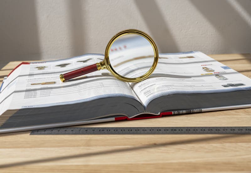 Golden magnifying glass over open thick technical book on desk. Concept of scientific study and research, finding stock photography