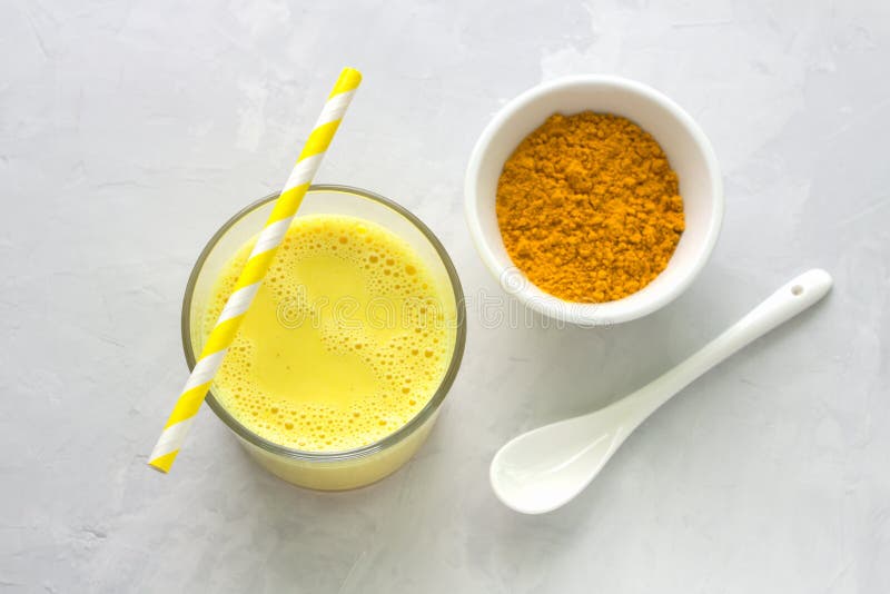 Golden milk with turmeric in a glass on a gray stone background