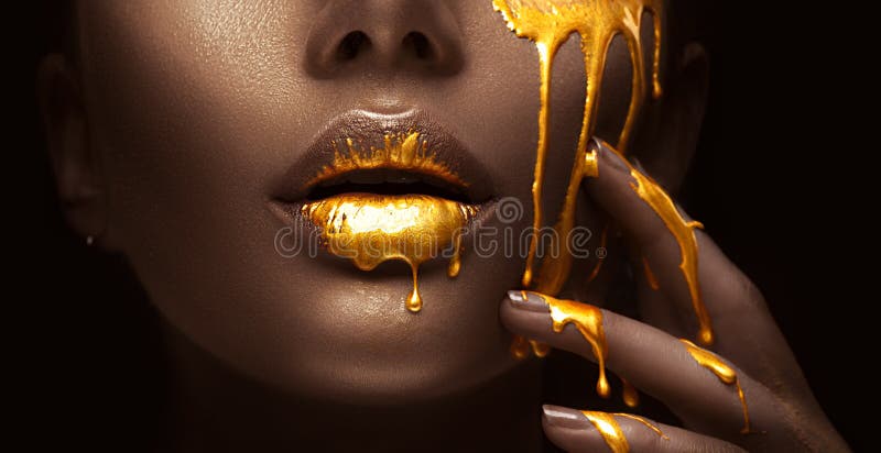 Golden paint smudges drips from the face lips and hand, golden liquid drops on beautiful model girl`s mouth, creative makeup