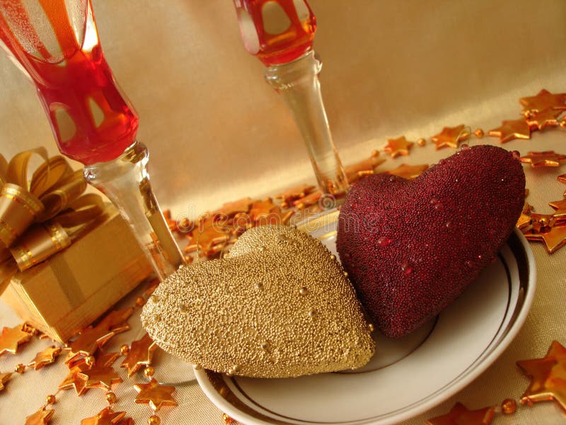 Golden and red hearts, gift box and glasses on celebratory table