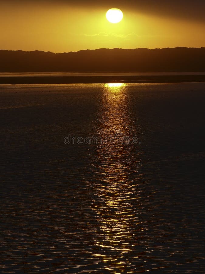 Il sole tramonta lentamente e si irradia riflessi dorati sull'acqua a Morro Bay, CA.