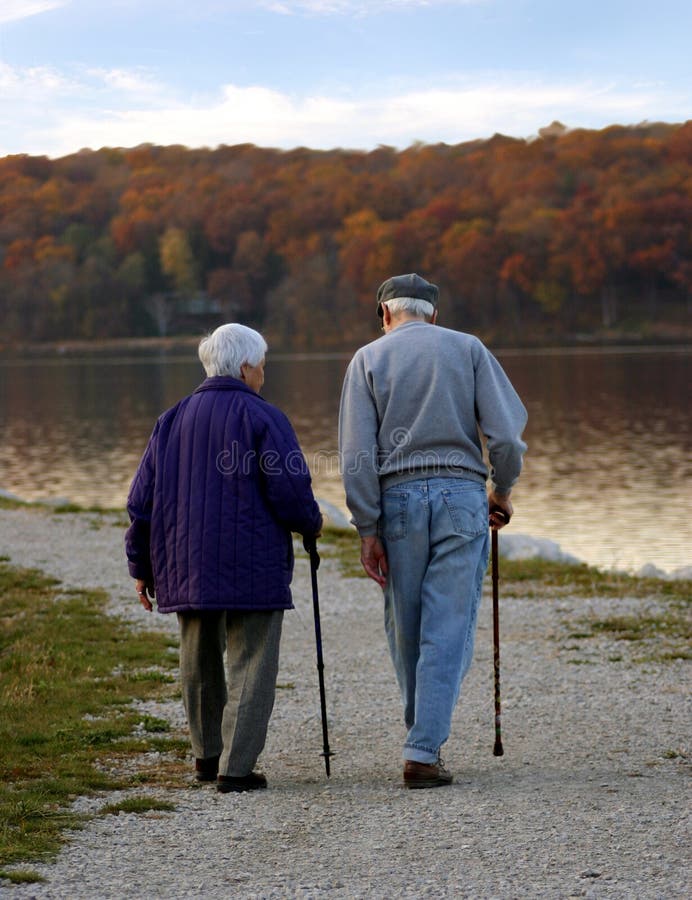 Starší manželský pár s holí, chůze po stezce vedle jezera na podzim.