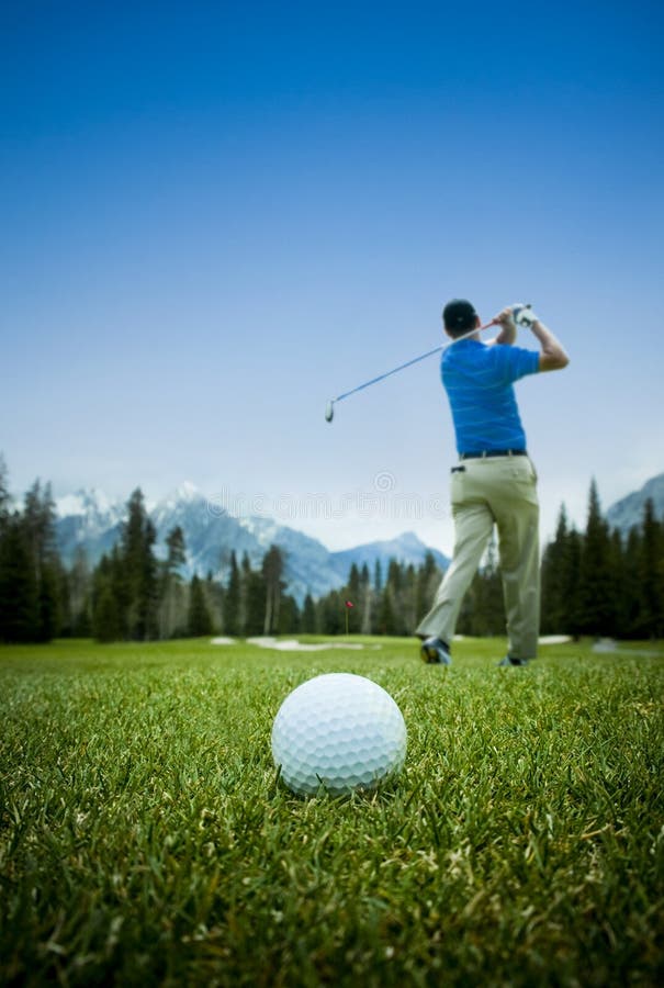 Golfista oscillante con palla da golf dietro di lui sul campo da golf, con il cielo azzurro e di montagna scape in estate.