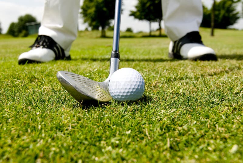 The picture shows feet, a golf club and a golf ball on a golf course