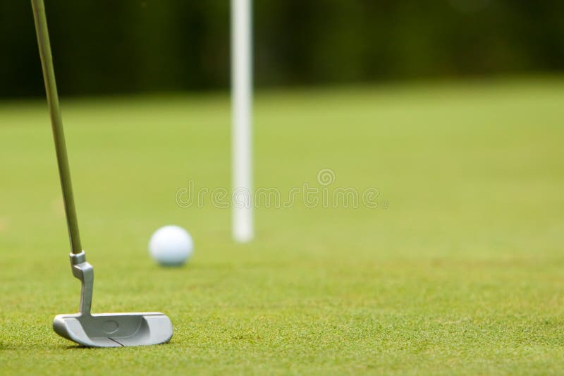 Golf ball and putter near green and flag