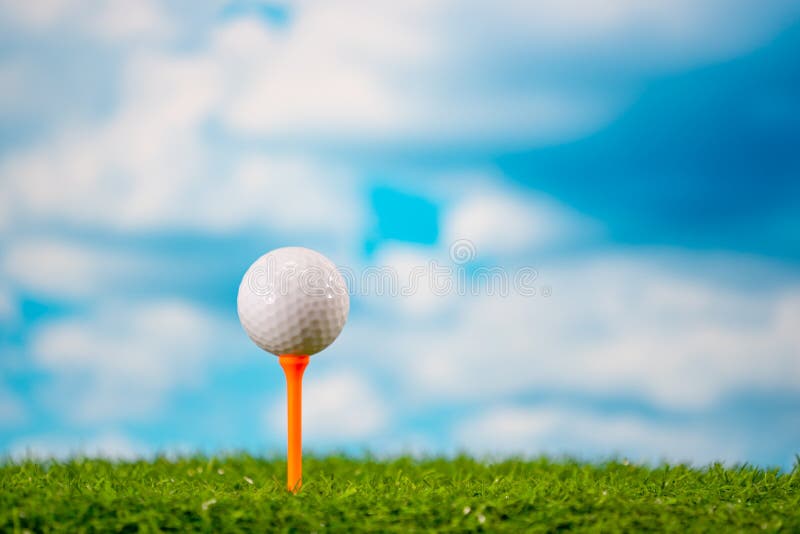 Golf ball on tee on grass on blue sky and cloud background