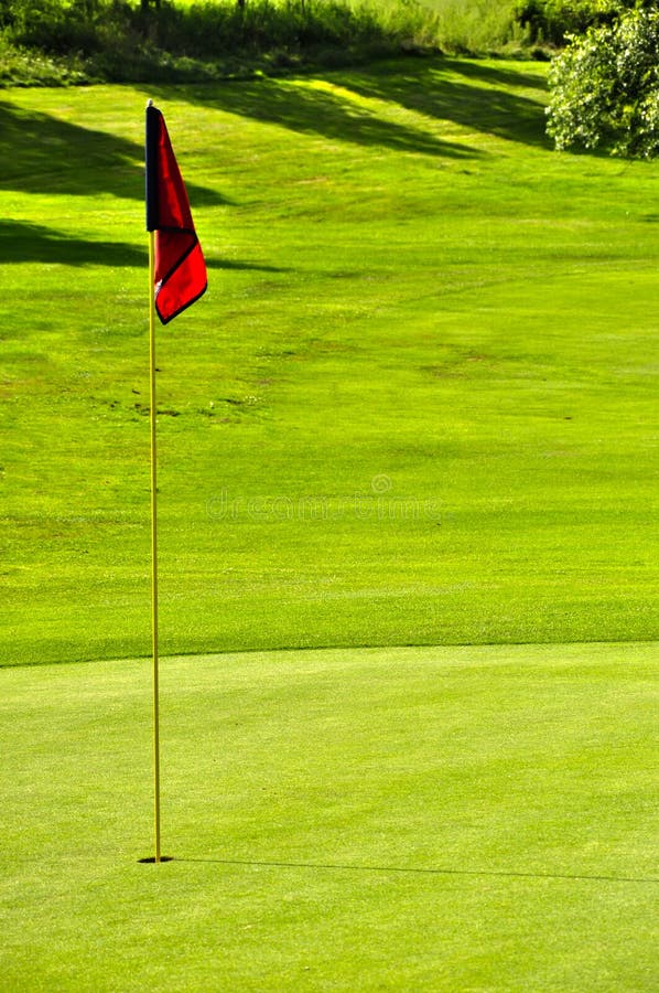 Golf field with a red flag hole and forest background in a sunny summer day. Golf field with a red flag hole and forest background in a sunny summer day