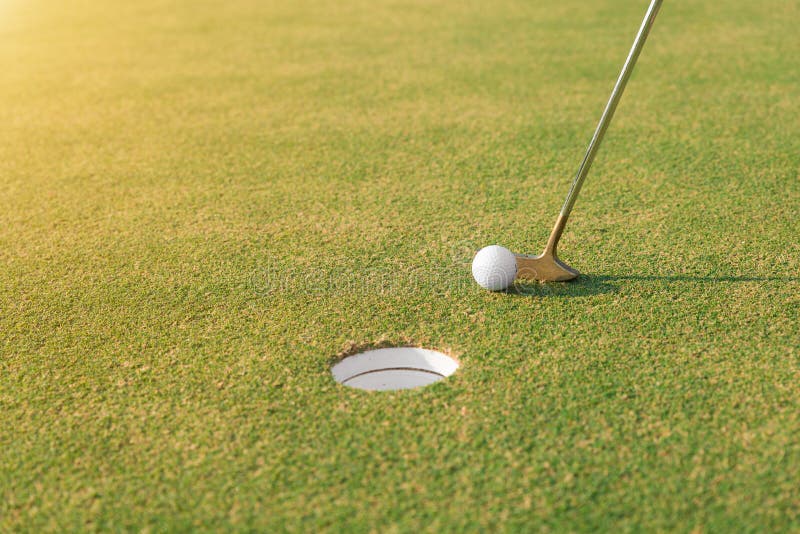 Golf player at the putting green hitting golf ball into a hole.