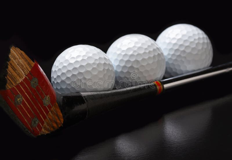 Golf Still Life. Three golf balls lined up along the shaft of an antique fairway wood. Closeup on black with reflection