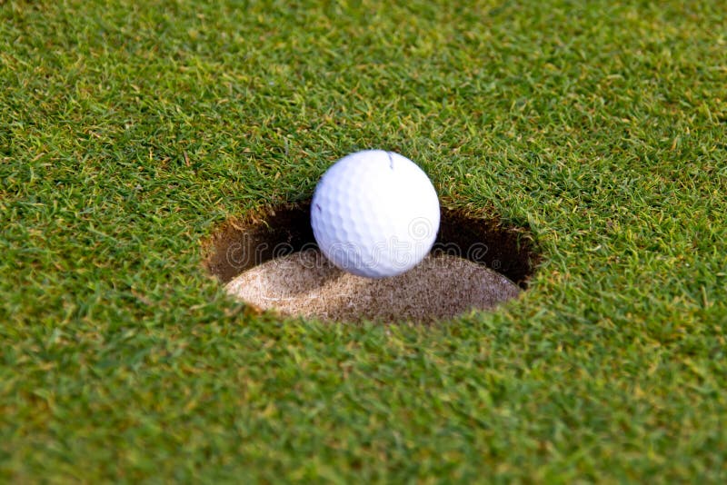 A golf ball is going in an hole. A golf ball is going in an hole