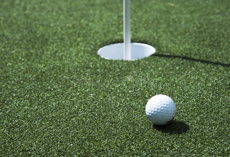 A golf ball sits near the hole on the putting green. A golf ball sits near the hole on the putting green