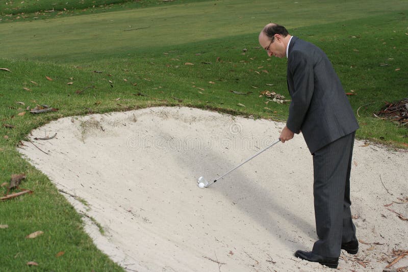 A golfer dressed in a business suit is about to hit a ball out of a sand trap. Theme: conducting business on a golf course. A golfer dressed in a business suit is about to hit a ball out of a sand trap. Theme: conducting business on a golf course.