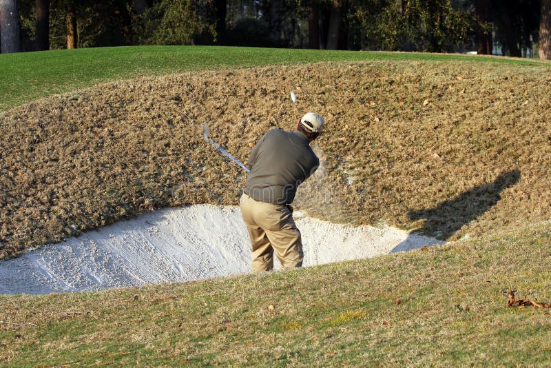 Golfer takes deep bunker shot.