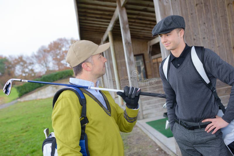 Golfing friends talking while holding clubs at golf course