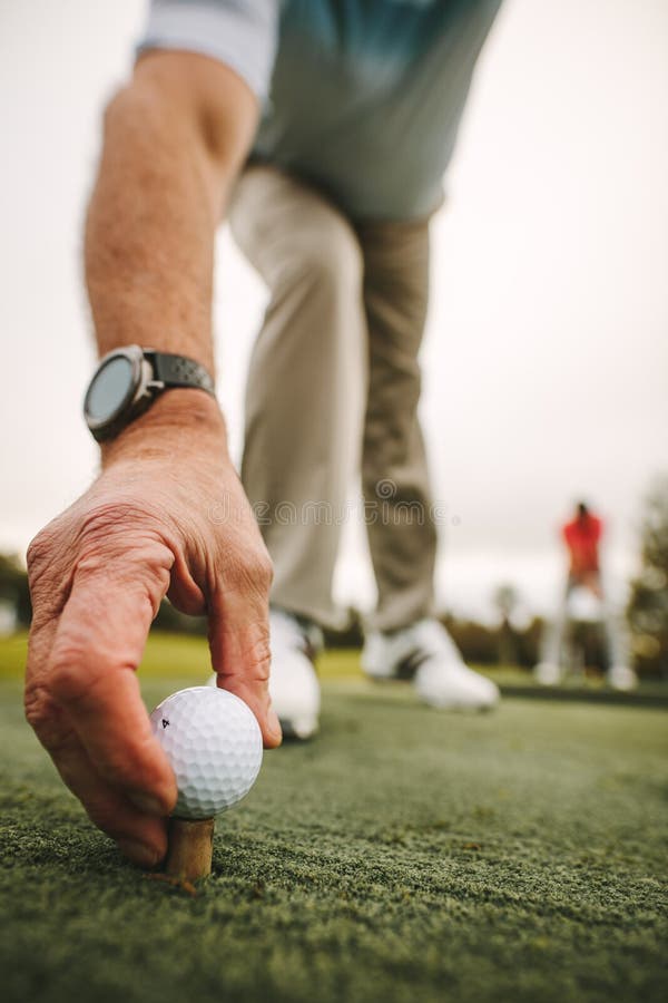 Golfspeler die golfbal plaatsen op T-stuk bij groen royalty-vrije stock foto's Golfspeler die golfbal plaatsen op T-stuk bij groen royalty-vrije stock foto's