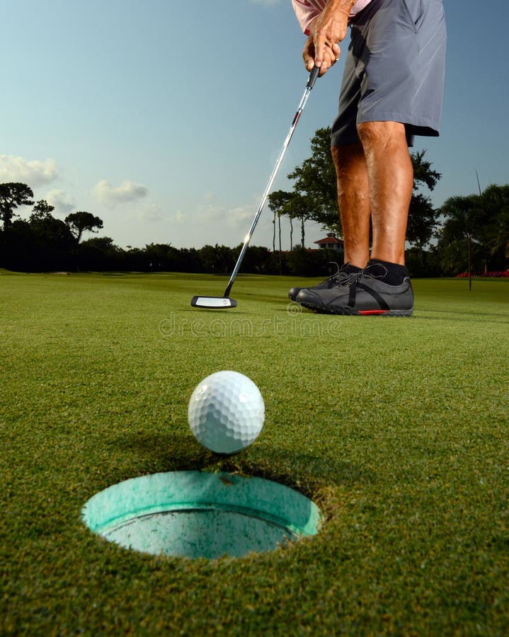 Golfer putting ball in hole on golf course. Golfer putting ball in hole on golf course