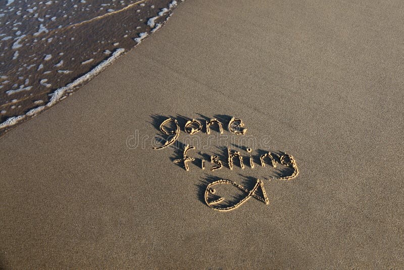 Gone fishing scritta nella sabbia della spiaggia con una piccola onda che lambisce i margini della scena.